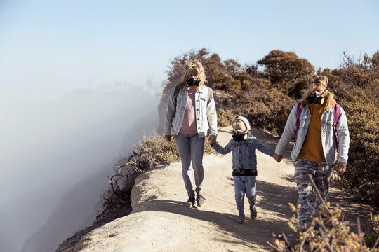 Family with respirator masks walking hand in hand along the edge of volcano Ijen, Java, Indonesia