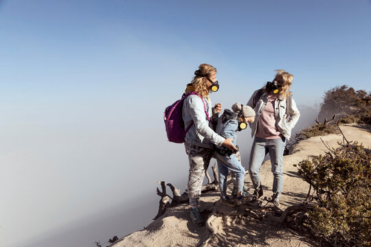 Family with respirator masks standing at the edge of volcano Ijen, Java, Indonesia