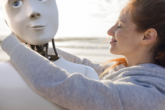Happy woman embracing robot on the beach