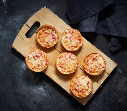 Cutting board and mini pizzas with cheese, tomatoes and ham