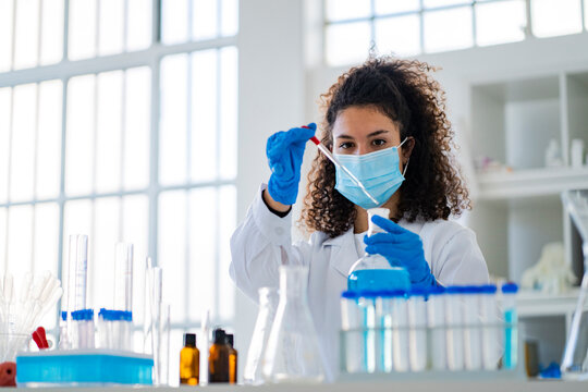 Young female doctor testing chemical solution in laboratory during COVID-19
