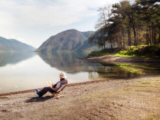 Italy, Lombardy, senior man sitting at Lake Idro using tablet