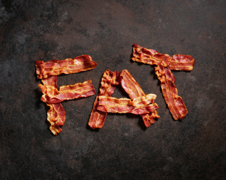 Bacon strips arranged in word FAT against metal surface
