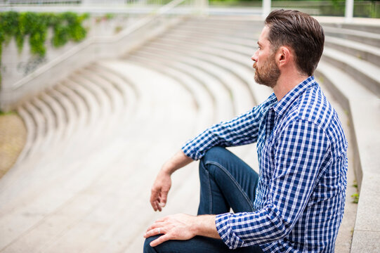 Side View Of Bearded Man Sitting On Amphitheater Steps In City