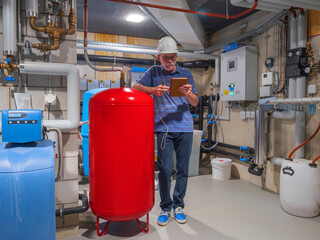 Senior craftsman checking water-processing unit, reading tablet