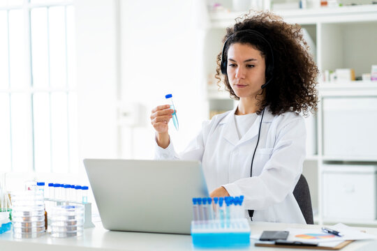 Female scientist with test tube working on laptop at clinic