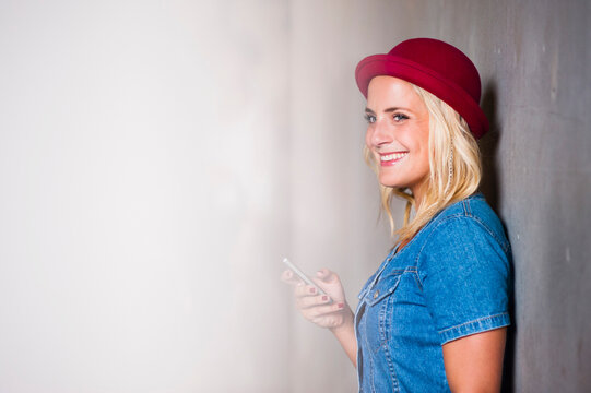 Portrait of happy young woman with smartphone leaning against wall