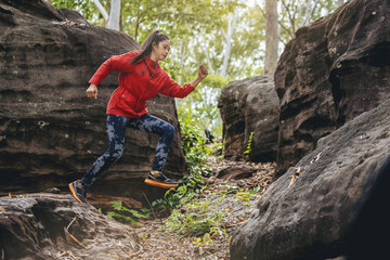 Naklejka premium Sport running woman in cross country trail run jumping on the rocky mountain path. 