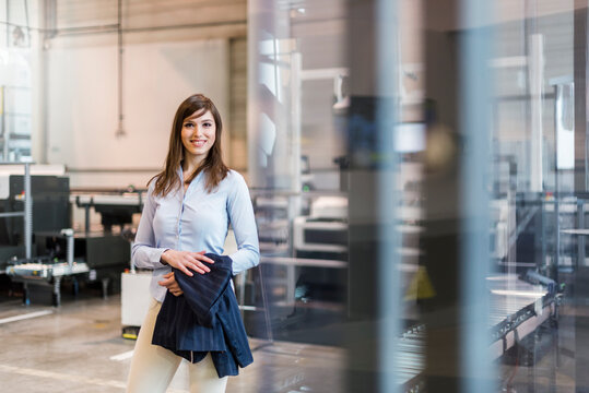 Smiling female professional holding blazer while standing in factory