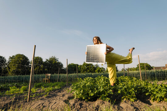 Young woman standing in a vegetable patch in the countryside holding solar panel