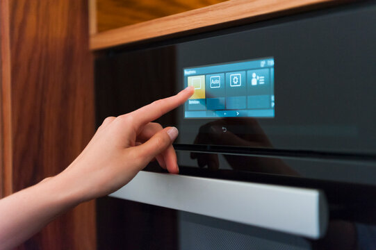 Woman hand touching oven's digital display in kitchen