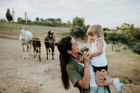 Smiling mother carrying cheerful daughter while standing against horses on land