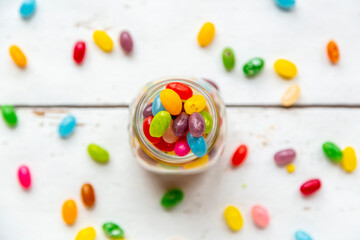 Glass of colourful sweet jellybeans on white wood