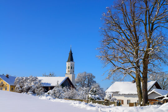 Church by snow covered landscape and bare tree against blue sky, Bavaria, Germany