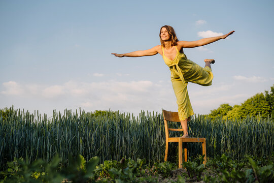 Young woman standing on a chair in the countryside pretending to fly