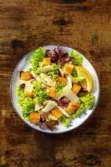 Caesar salad, shot from the top on a dark rustic wooden background. Lettuce leaves, crispy croutons and chicken meat, with a place for text