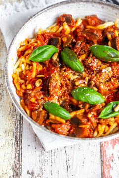 Bowl of pasta with aubergine tomato sugo garnished with pine nuts, parmesan and basil