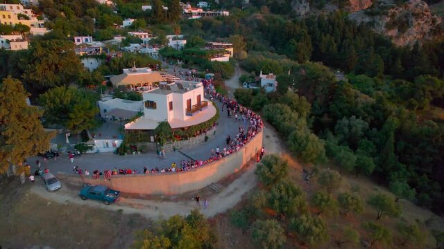 Crowd of people on village street enjoy sunset, aerial pullback