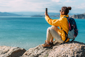 A traveler takes a selfie on her phone against the background of the sea, Close-up. Travel and active lifestyle concept. A woman holds a phone in her hands against the background of the blue sea.
