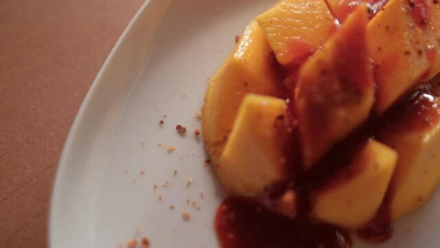 Plate of chopped mango with Mexican chamoy sauce and blurry background