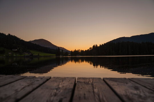Mountains reflecting in shiny lake at dusk with edge of jetty in foreground