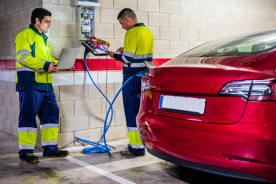 Male technicians working by meter while charging electric car in auto repair shop