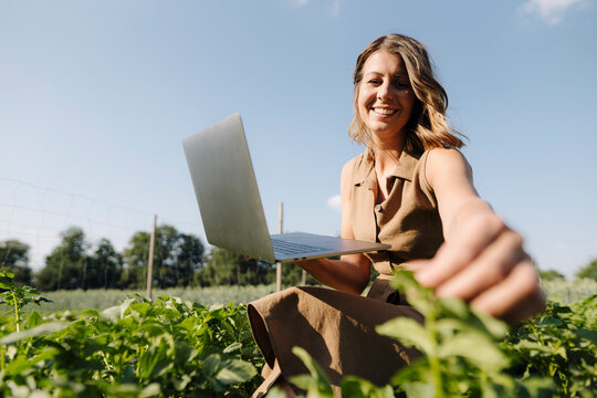Young woman with laptop caring for plants in a vegetable patch
