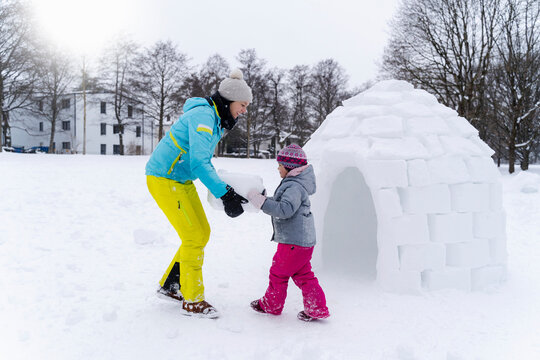 Girl with help of mother carrying snow block to build igloo at park
