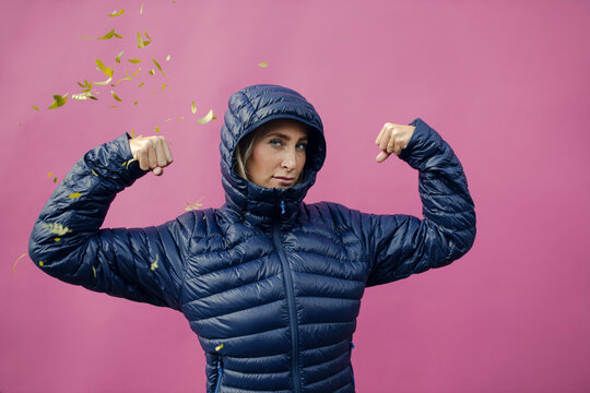 Young woman flexing muscles against purple wall