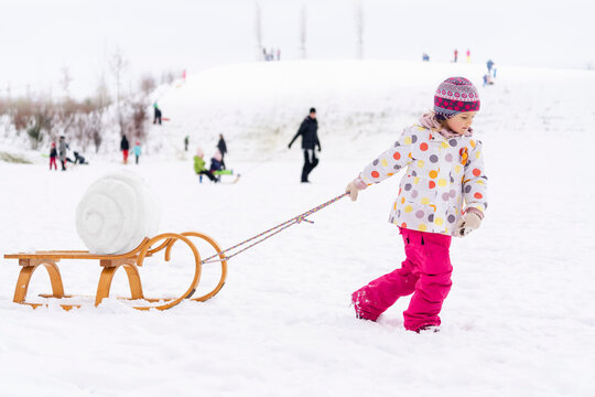 Girl in warm clothing pulling sled on snow at park
