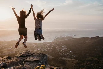 Tuinposter South Africa, Cape Town, Kloof Nek, two women jumping on rock at sunset © letizia haessig photography/Westend61