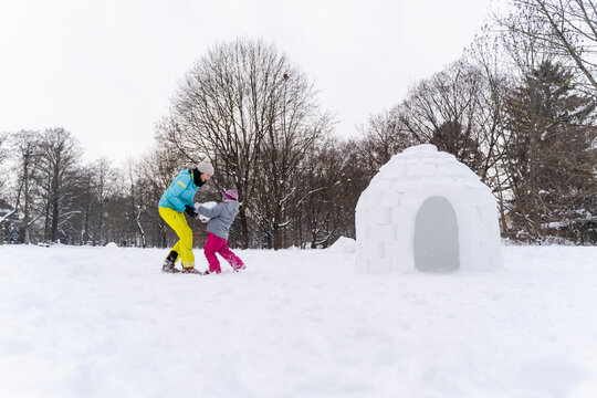 Mother and daughter carrying snow block to build igloo at park against bare trees