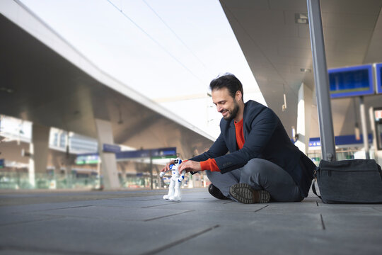 Smiling entrepreneur looking at robot while sitting on railroad platform