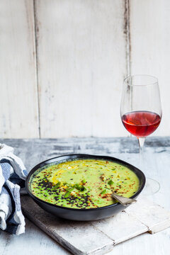 Bowl of Fresh green pea soup with spring onions and a glass of blush Wine