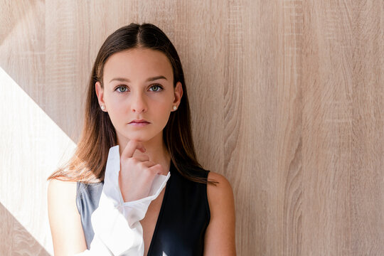 Teenage girl wearing sleeveless top with white jacket against wooden wall at home