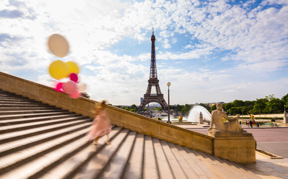 Woman with balloons climbing down staircase against Eiffel Tower in Paris, France