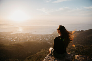 Naklejka na ściany i meble South Africa, Cape Town, Kloof Nek, woman sitting on rock at sunset