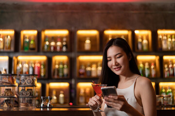 Nightlife concept a sexy girl with smiling face checking messages in her smartphone with a vivid pink champaign in her hand