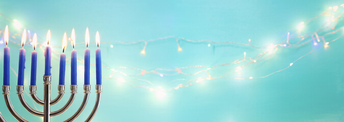 Image of jewish holiday Hanukkah with menorah (traditional candelabra) and candles over garland glitter lights background