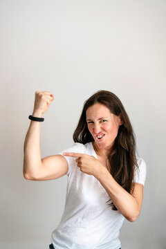 Portrait of cheerful mature woman pointing at bicep against white background