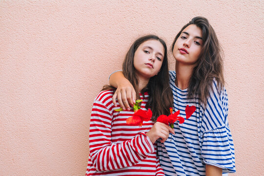 Sisters holding hibiscus flowers while standing against wall