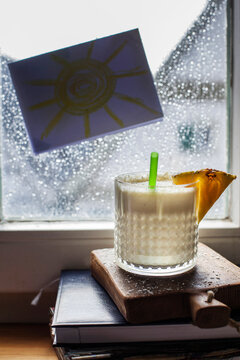 Glass of Pina Colada standing in front of window covered in raindrops