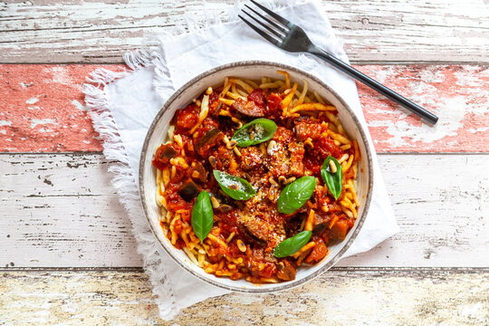 Bowl of pasta with aubergine tomato sugo garnished with pine nuts, parmesan and basil