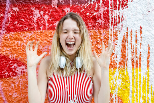 Cheerful woman with eyes closed shouting against multi colored wall