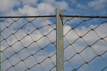 wire stainless steel net made of ropes connected by metal connectors as a fence filling, loops, rope connectors, protective protective filling in the garden, galvanized, zinc, blue sky, end, lawn