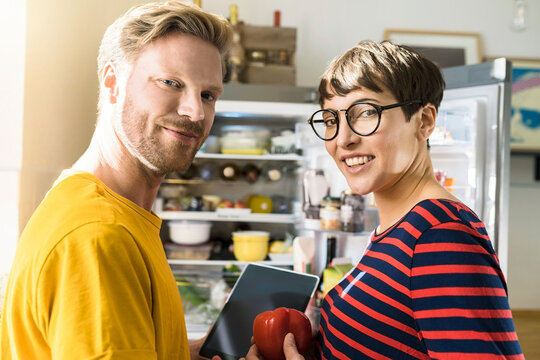 Portrait of couple with tablet in front of their fridge doing online shopping for groceries
