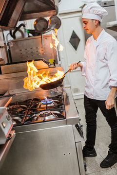 Junior chef with pan of flames in traditional spanish restaurant kitchen