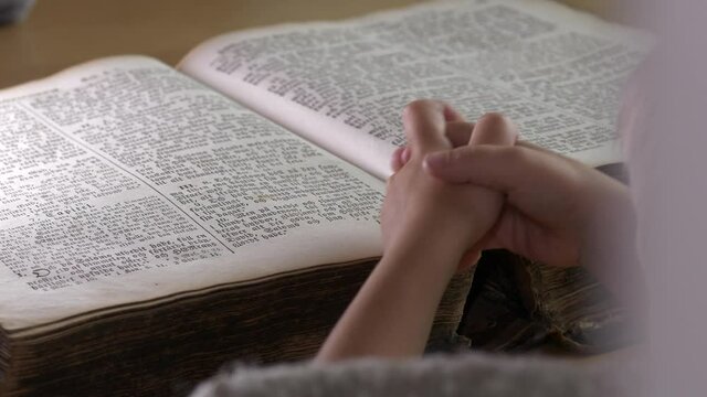 Clasped hands of child praying on Scripture book. Static view
