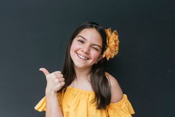 Close-up of smiling girl wearing headband showing thumbs up against black background