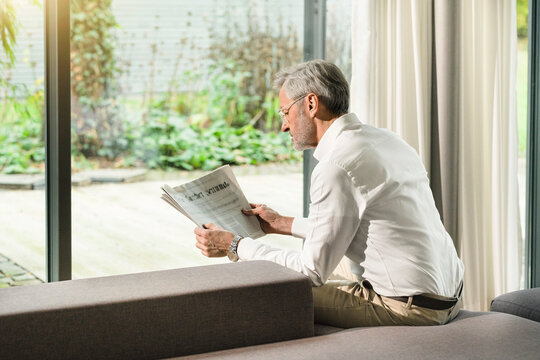 Senior man with grey hair in modern design living room reading newspaper